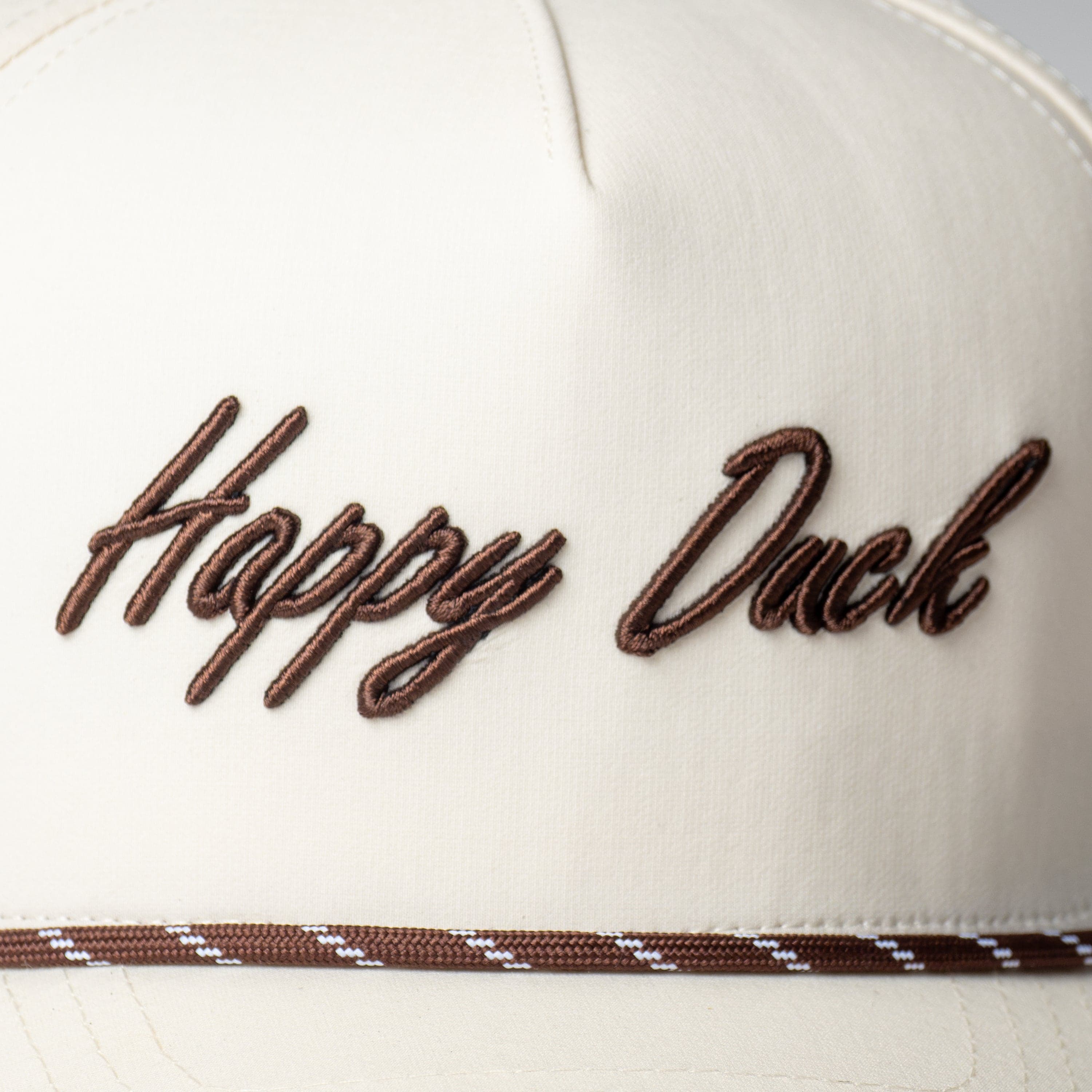 Close-up of the embroidered Happy Duck script logo on cap fabric